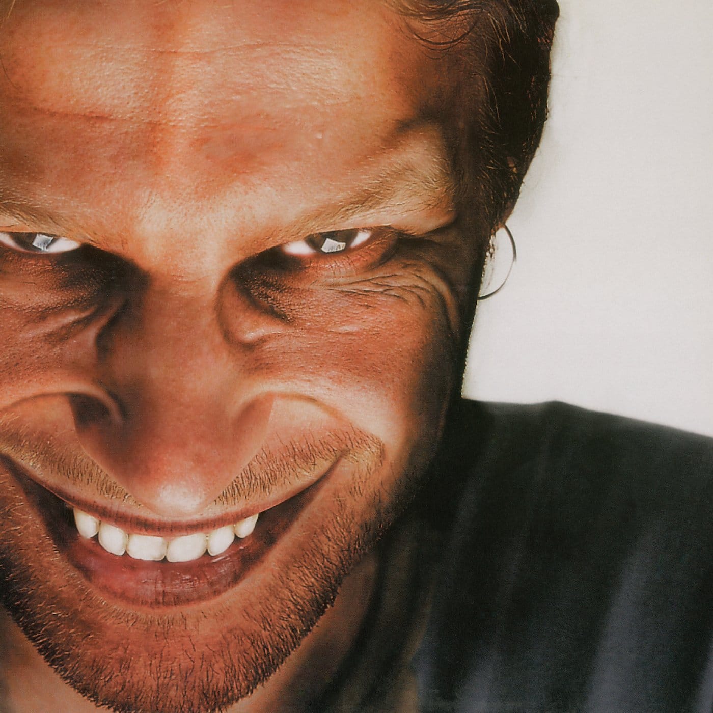 High-contrast close-up of Aphex Twin's grinning face against a white background, on the Richard D. James Album cover.